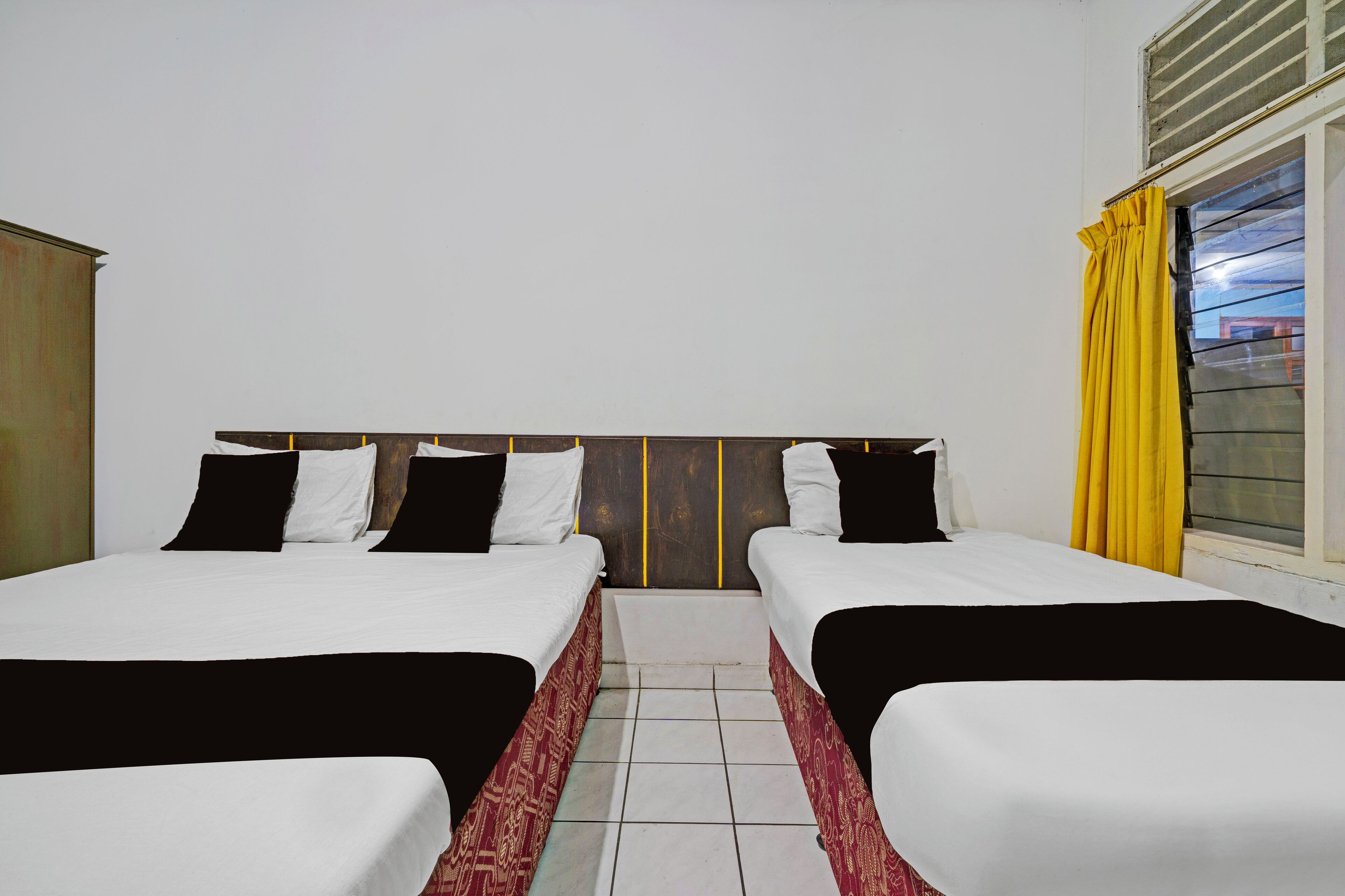 A hotel room with two beds, a wooden headboard, a window with yellow curtains, and a tiled floor.