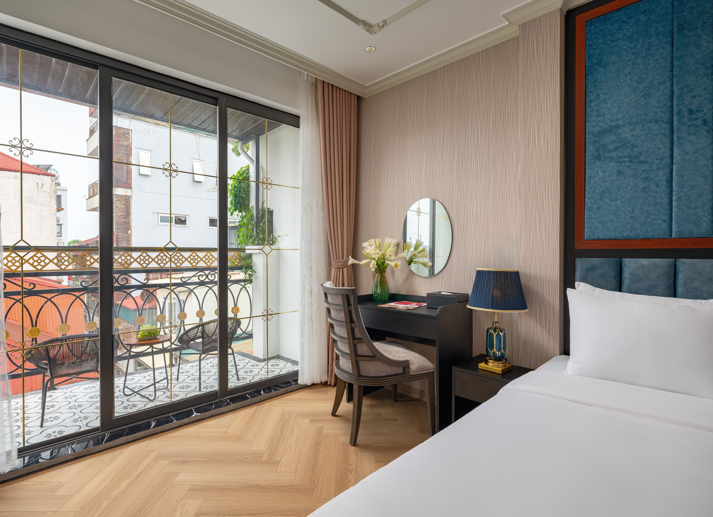 A hotel room with a large window, a desk with a chair, a bed, and a nightstand with a lamp.