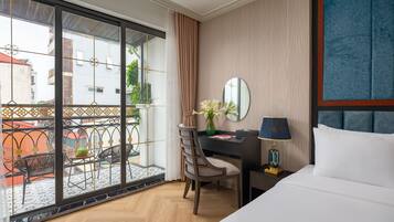 A hotel room with a large window, a desk with a chair, a bed, and a nightstand with a lamp.