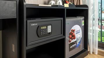 A hotel room with a minibar, a digital safe, and a refrigerator with a beverage advertisement.