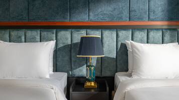 A hotel room with two beds, a dark headboard, a nightstand with a lamp, and a wooden accent strip.