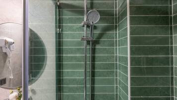 Ett badrum med en dusch som är avskärmad med glasväggar, ett duschmunstycke som kan hållas i handen, en väggmonterad blandare och en handdukshängare med handdukar.