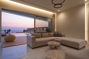 A modern living room with a large sectional sofa, a round coffee table, and a view of the sea.