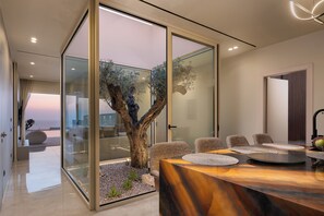 Ein modernes Interieur mit Essbereich, der einen Holztisch und -stühle, eine Glastrennwand mit Blick ins Freie sowie eine große Holzskulptur umfasst.