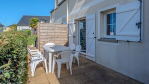 A patio area with a table and chairs, a wooden fence, and a building with white shutters.