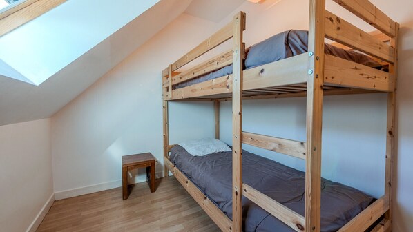 Een slaapkamer met twee stapelbedden, een klein houten krukje en een dakraam.