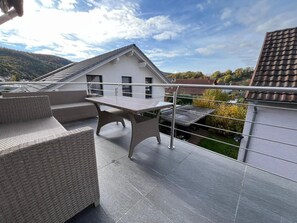 Una terraza en la azotea con mobiliario exterior, vista a un edificio blanco y un paisaje montañoso al fondo.