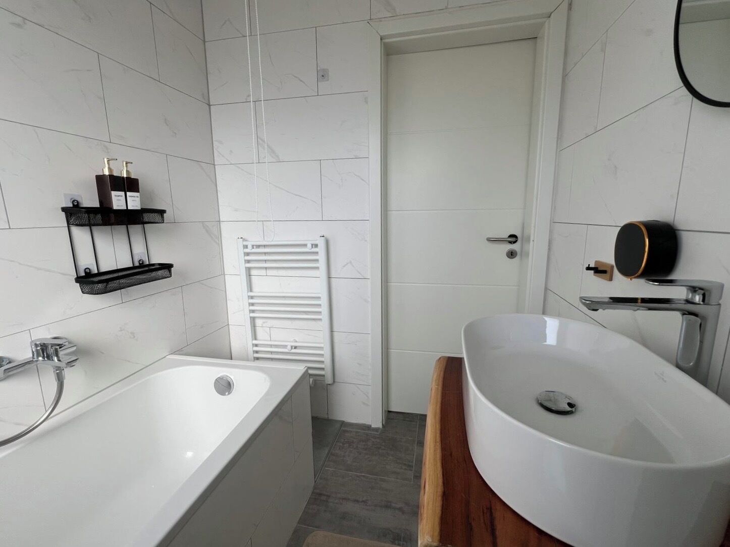 A modern bathroom with a freestanding bathtub, a white sink with a wooden vanity, and a towel rack on the wall.