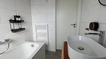 A modern bathroom with a freestanding bathtub, a white sink with a wooden vanity, and a towel rack on the wall.