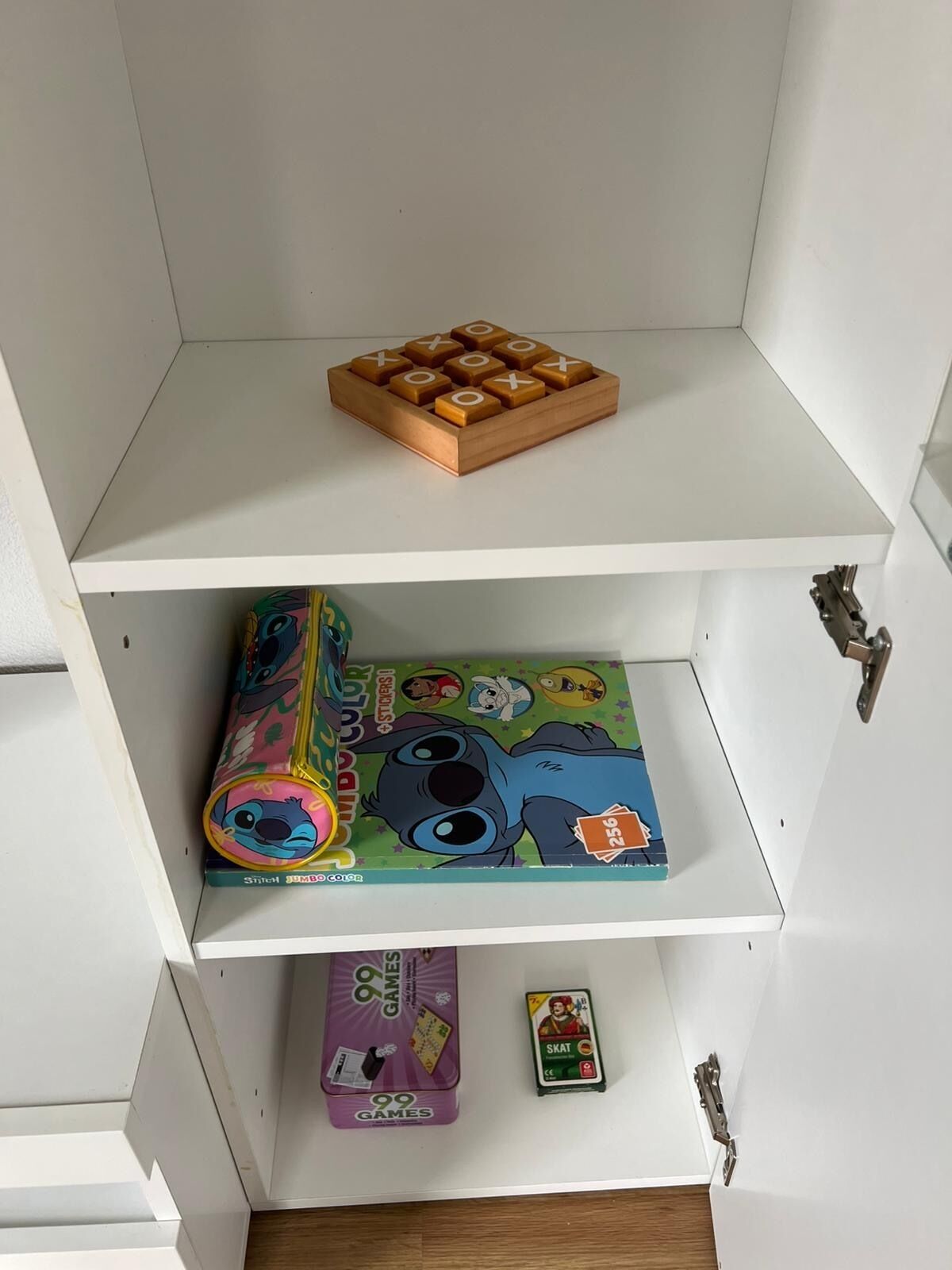 Een plank met een houten variant van tic-tac-toe, een kleurrijke doos van Stitch en een bordspel met Stitch-thema, plus een kleine doos voor het kaartspel Skat.