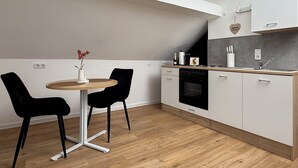 Et moderne køkken med hvide skabe, en træbordplade, en sort ovn og et lille spisebord med to stole.