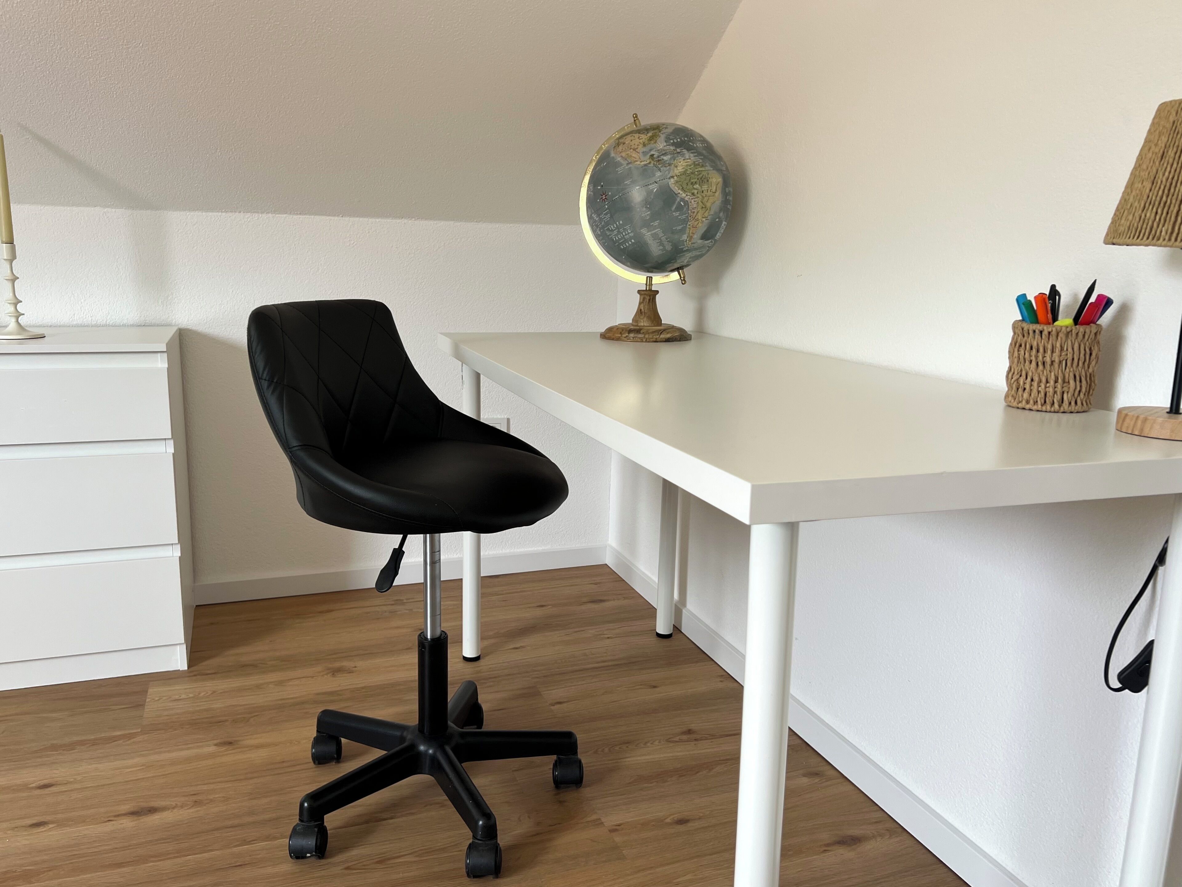 A modern office space with a white desk, black office chair, globe, and a basket of pens.