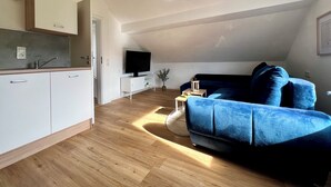 En moderne lejlighed med et køkken, en stue med en blå sofa og et fjernsyn.