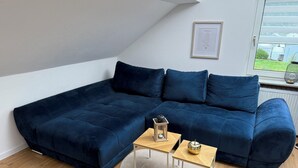 En moderne stue med en mørkeblå hjørnesofa, et lille træsofabord og et indrammet kunstværk på væggen.
