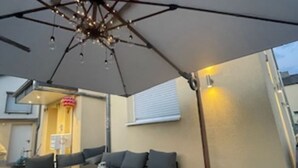 Un espace extérieur aménagé en terrasse, avec une table et des chaises, un grand parasol et un canapé.