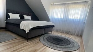 Une chambre à coucher avec un lit, un ventilateur de plafond et une grande fenêtre ornée de rideaux légers.