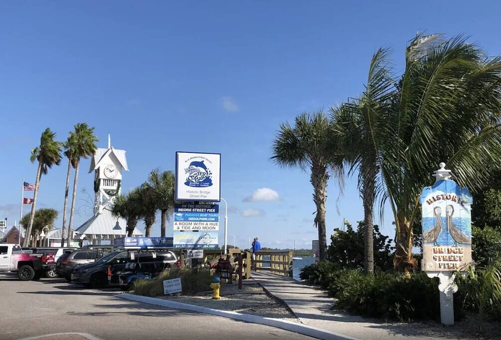 A historic bridge street pier with a clock tower, palm trees, and a signboard advertising tours and a room with a view.