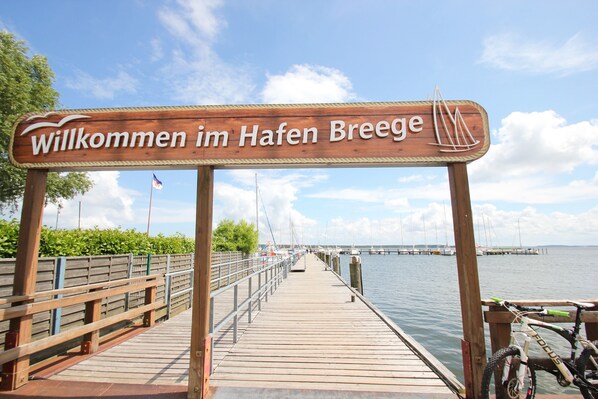 Une promenade en bois mène à un plan d’eau, et une pancarte indique : « Bienvenue au port de Breesge ».