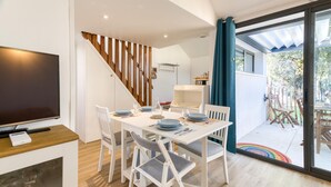 A modern dining area with a wooden staircase, a TV, and a view of the outdoors. - Maison accès plage direct (Meschers-sur-Gironde)