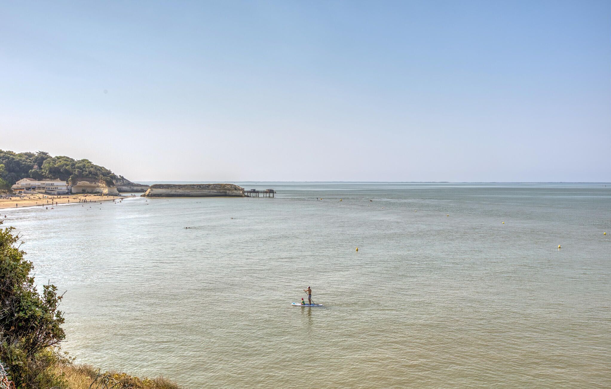 Escena costera con una playa, un muelle y afloramientos rocosos.