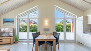 A dining area with a wooden table and chairs, large windows, and a view of a house.