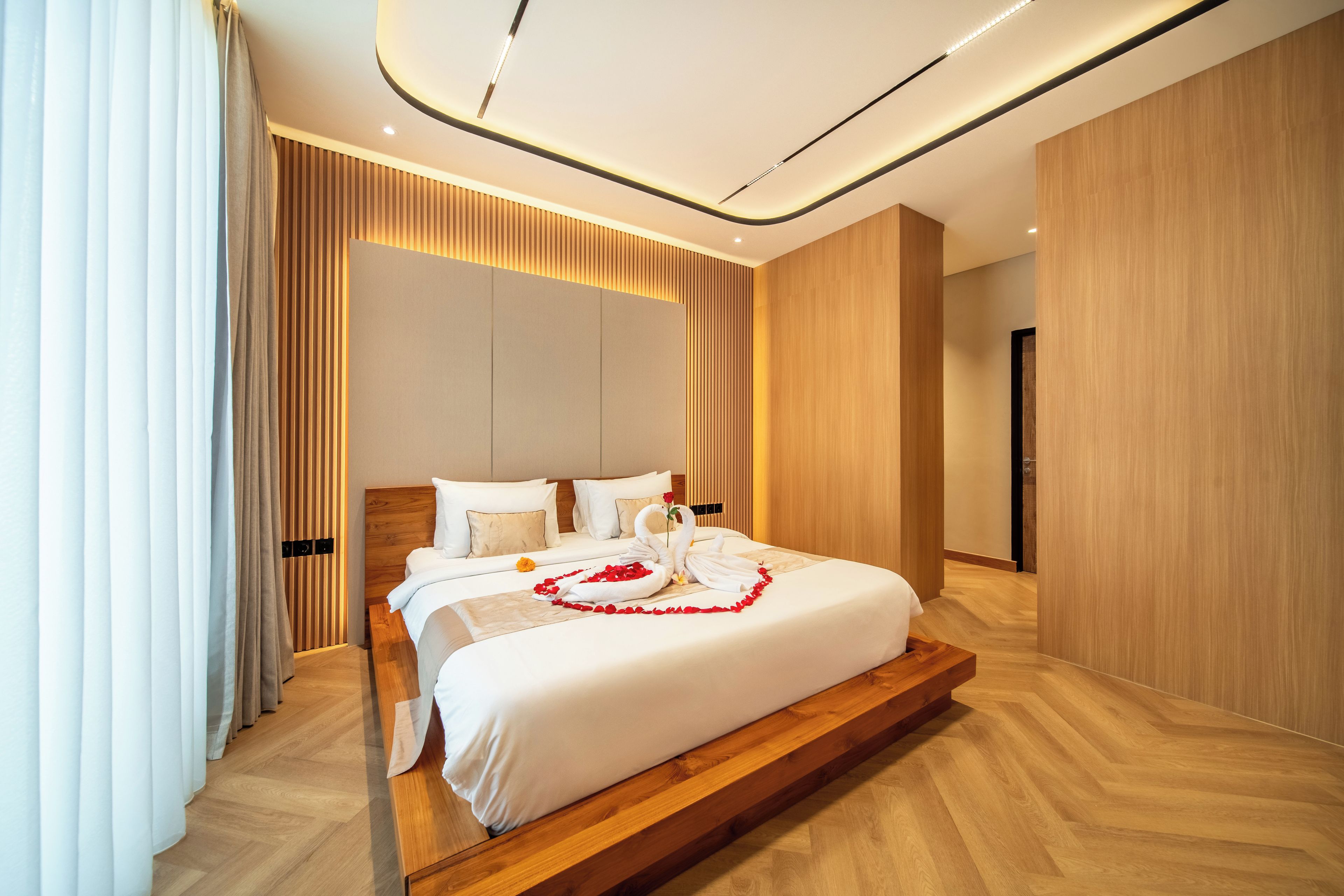 A modern hotel room with a large bed, wooden flooring, and a neutral color palette.