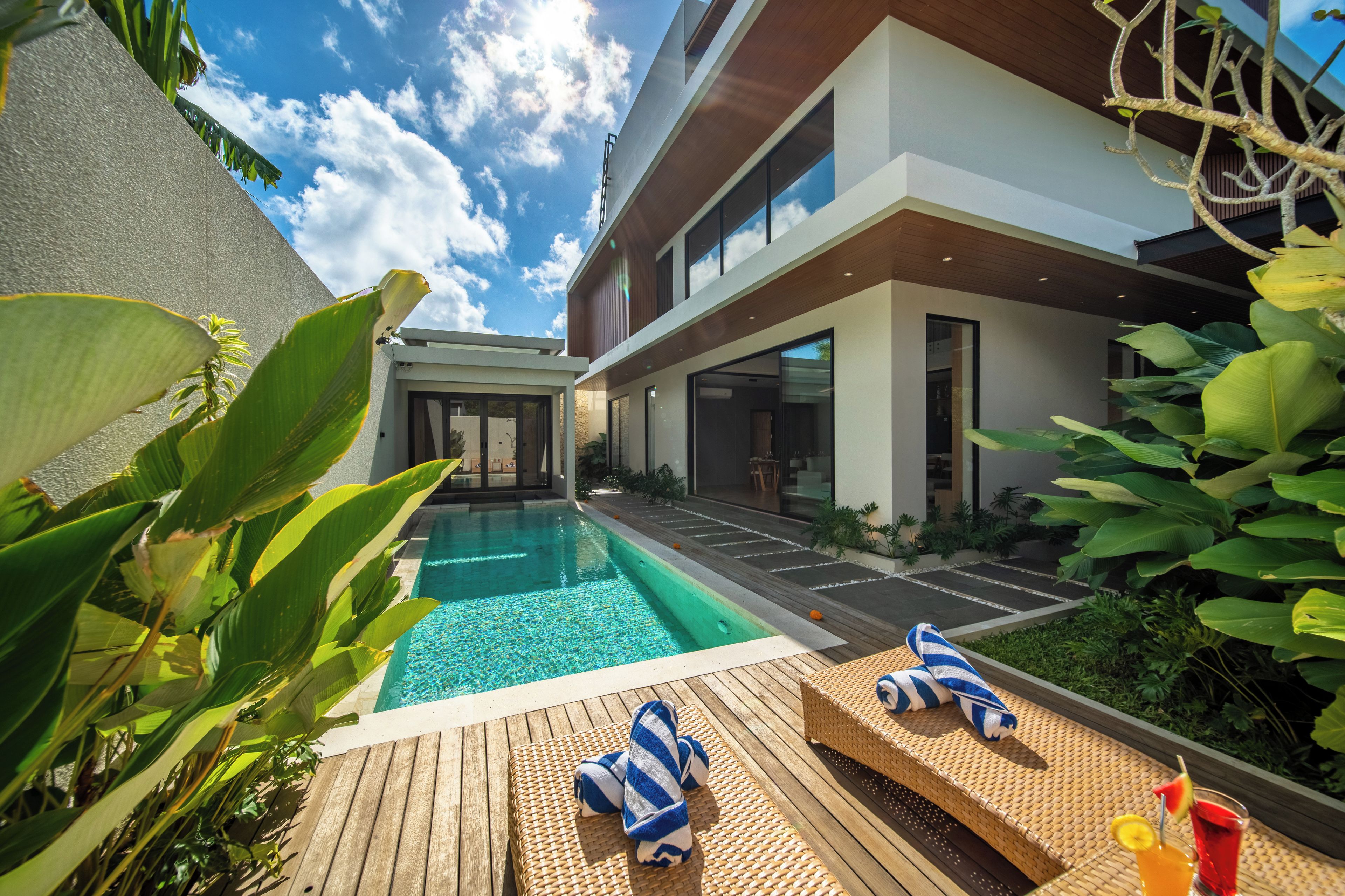 A modern house with a swimming pool, wooden deck, and lounge chairs.