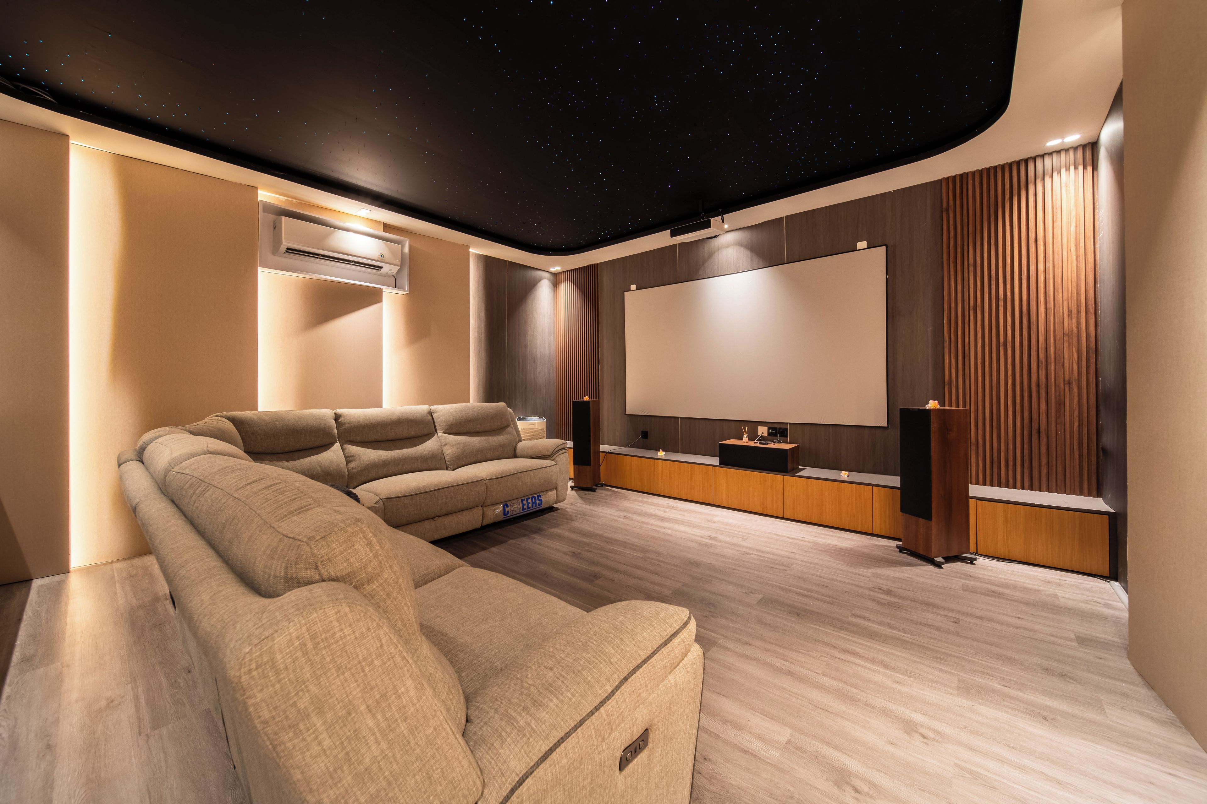 Een moderne thuisbioscoopruimte met een groot flatscreen televisietoestel, een comfortabele bank en een sterrenhemel ontwerp aan het plafond.