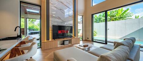 A modern living room with a large TV screen displaying 'NETFLIX,' a sofa, a coffee table, and a view of a swimming pool.
