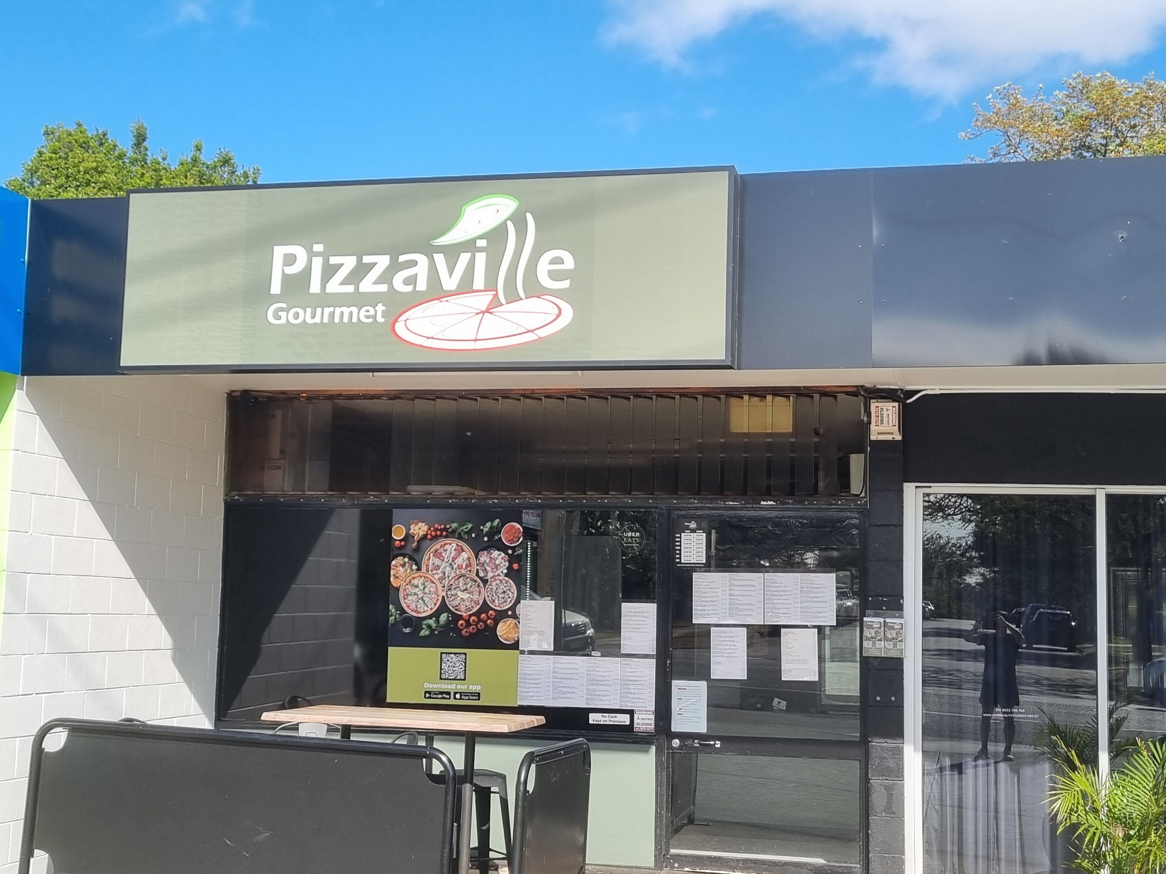 En butik med et skilt, der siger "Pizzaville Gourmet", og en menutavle udenfor.