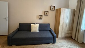 Uma sala de estar moderna com um sofá escuro, uma almofada clara e três prateleiras pequenas fixadas na parede com objetos decorativos.
