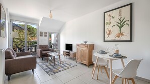 Una sala moderna con sofá, sillón, mesa de centro y mesa de comedor. Hay un televisor, mueble aparador y una obra de arte en la pared.