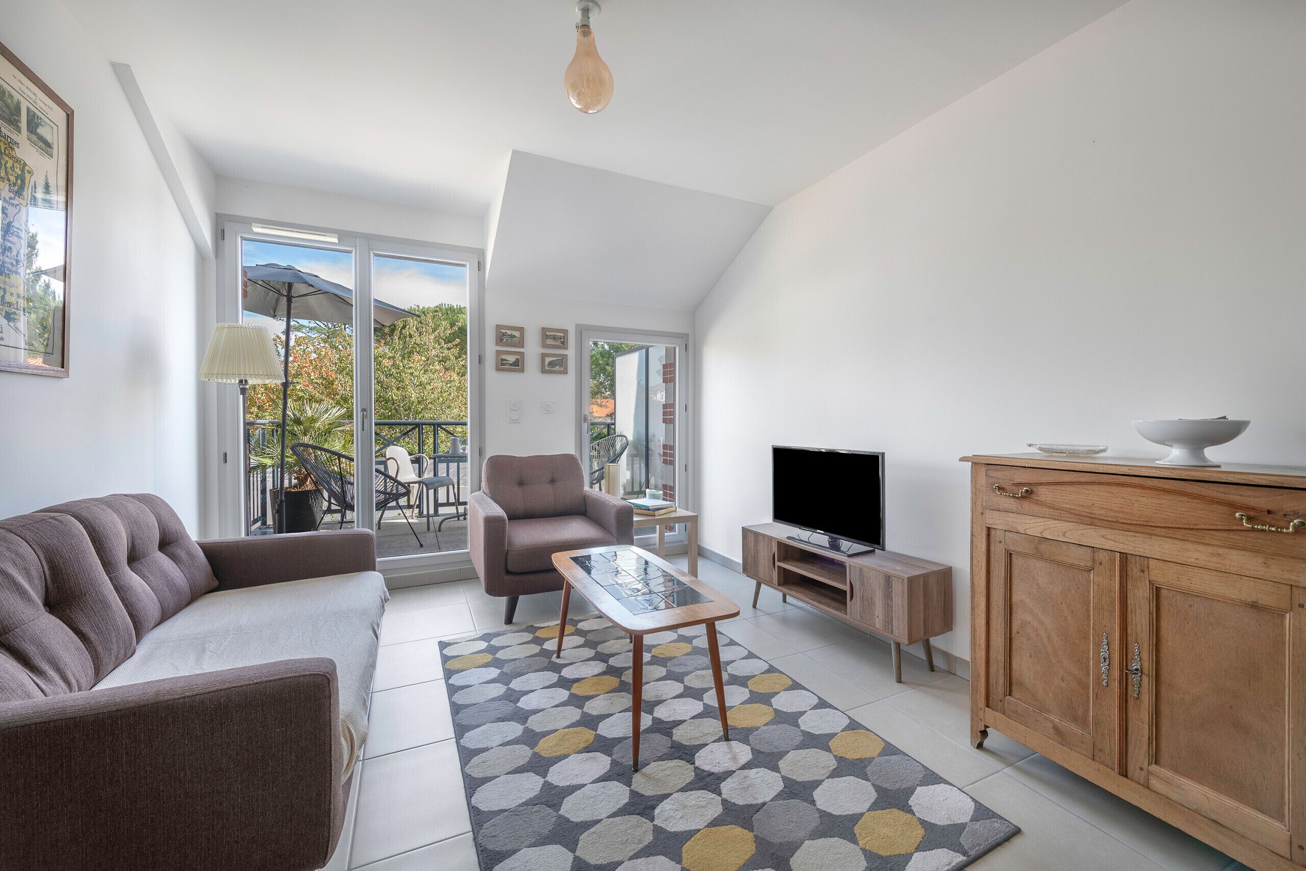 En moderne stue med sofa, lænestol, sofabord, fjernsyn, træskab og et mønstret tæppe.