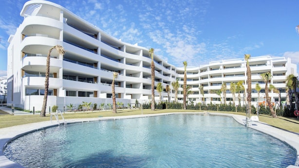 Un hôtel moderne doté d’une grande piscine, de nombreux balcons et de palmiers.