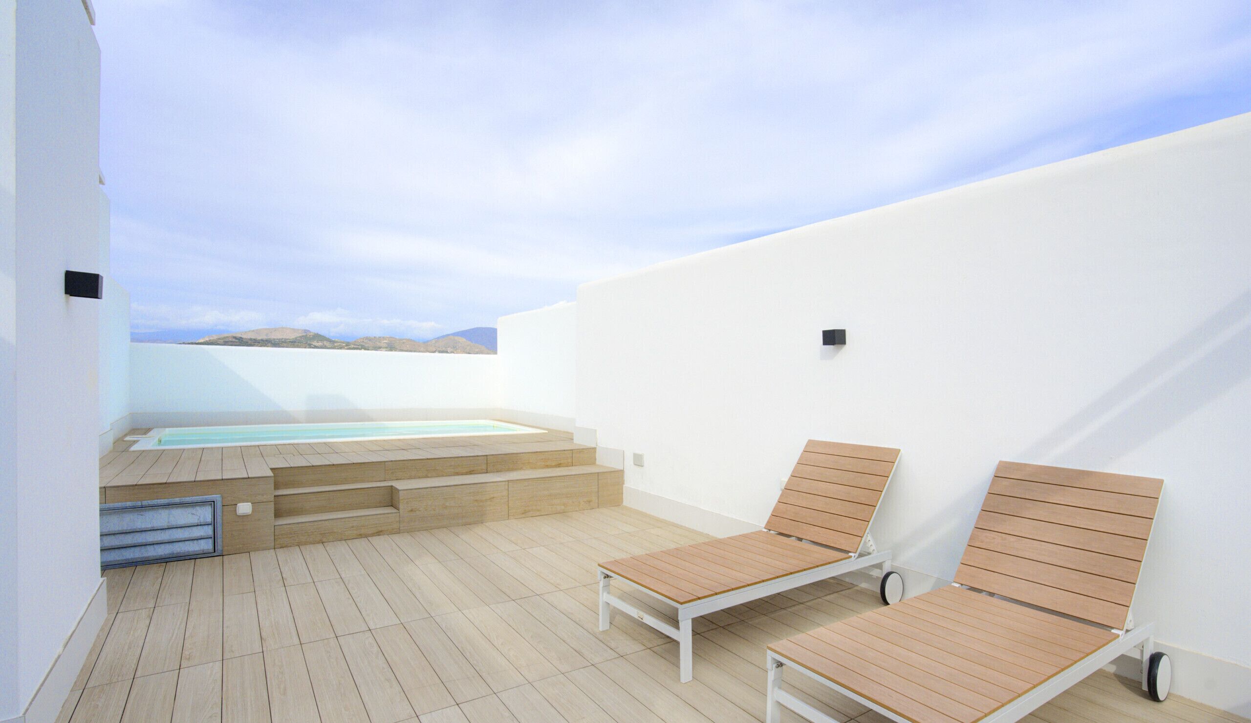 Una terraza en la azotea con piscina, dos sillones de descanso y vistas al mar.