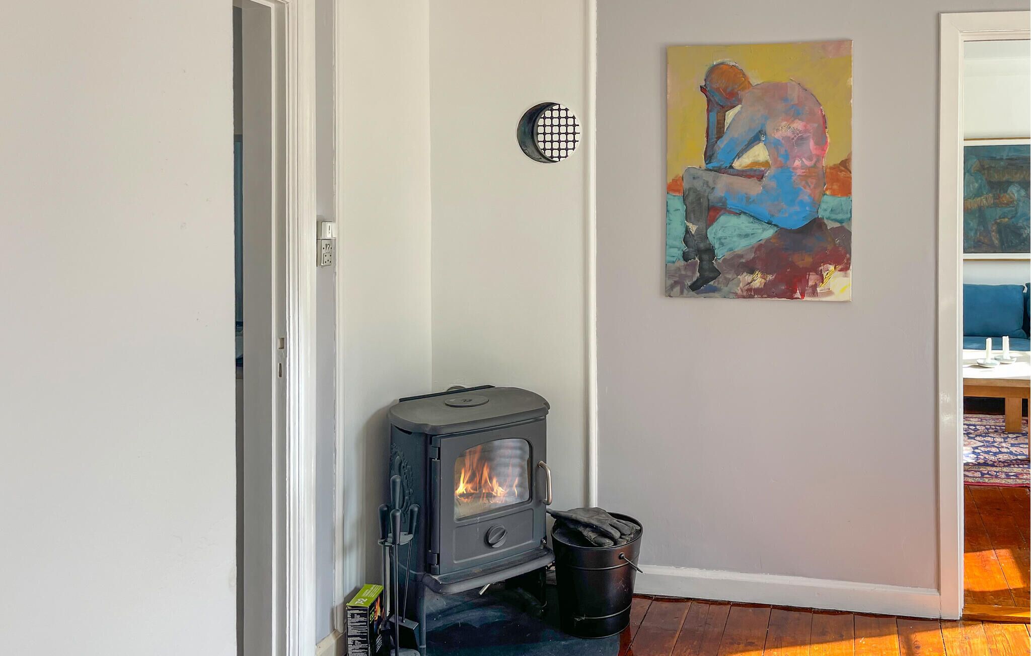 A room with a wood-burning stove, a painting on the wall, and a door with a power outlet.