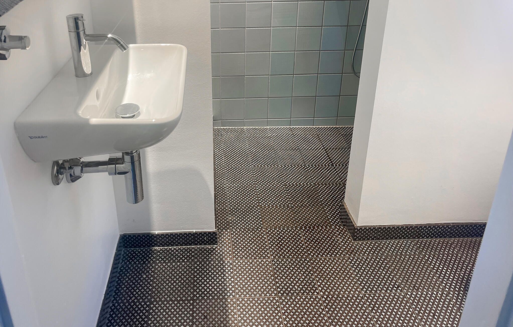 Een badkamer met een witte wastafel, een betegelde vloer en een douchehoek.
