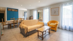 A living room with a sofa, a coffee table, a dining table with chairs, a blue cabinet, and a window with curtains.