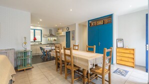 A dining area with a table set for four, a kitchen in the background, and a blue door.