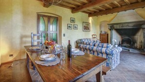 Un coin repas avec une table en bois dressée pour le repas, un canapé à motifs floraux et une cheminée en arrière-plan.