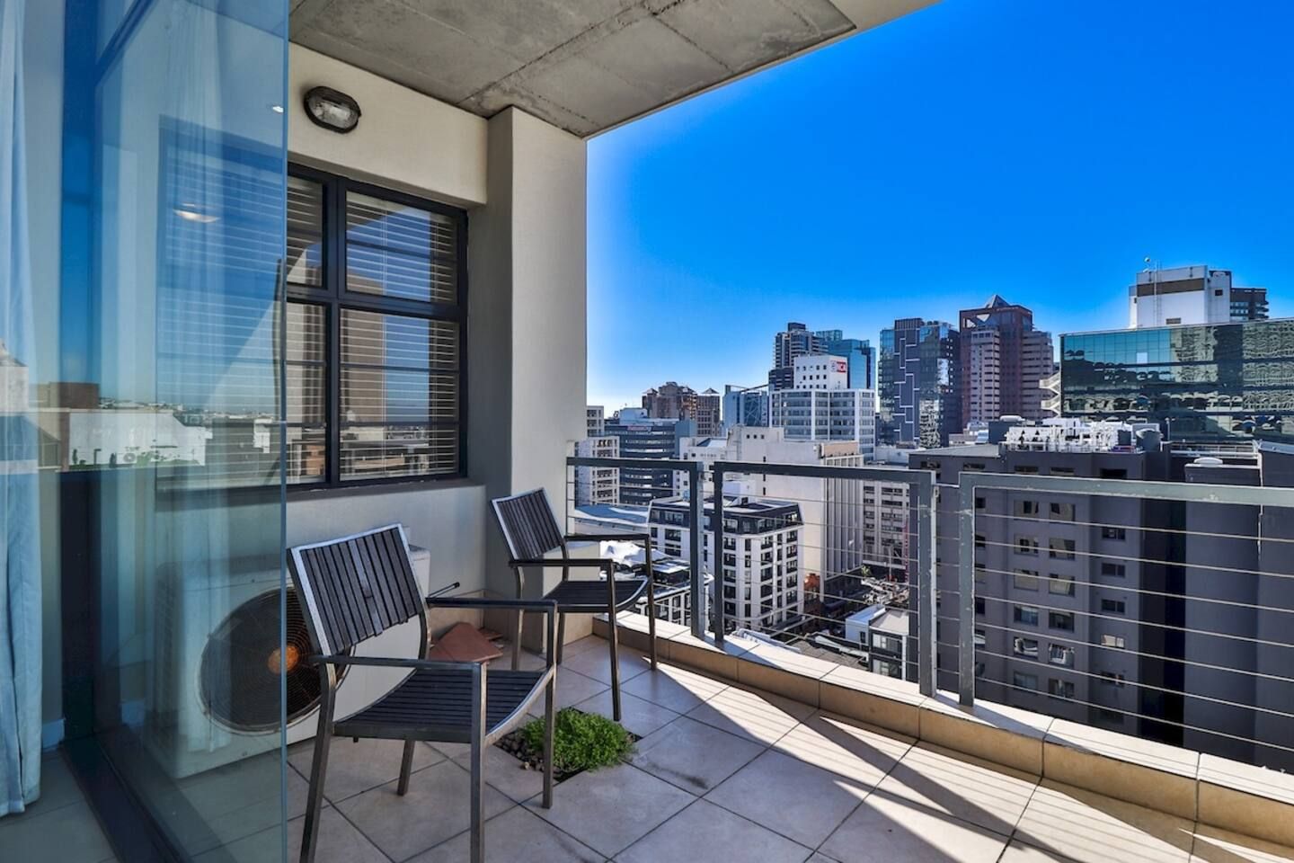 A balcony with two chairs and a table, overlooking a cityscape with modern buildings.
