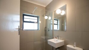Et badeværelse med bruser, håndvask, toilet og et vindue.