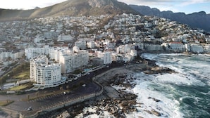 A coastal cityscape with a prominent mountain in the background, a beachfront, and residential buildings. - Spring Tide Inn - Standard Family Room 2 (Cape Town)