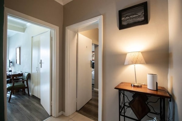 A hallway with a dining area visible through an open door, a lamp on a table, and a framed picture on the wall.