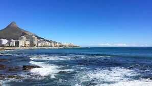 A coastal cityscape with a prominent mountain, buildings along the shore, and rough sea waves. - Spring Tide Inn - Standard Family Room 2 (Cape Town)