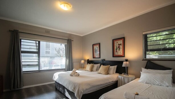 Et hotelværelse med to senge, et stort vindue med skodder, en loftslampe og kunst på væggene.