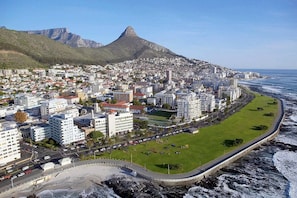 A coastal cityscape with a prominent mountain in the background, a beachfront promenade, and dense urban development.