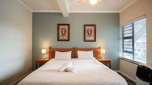 A hotel room with a bed, two bedside lamps, a ceiling fan, and two framed pictures on the wall. - Spring Tide Inn - Standard king room 3 (Cape Town)