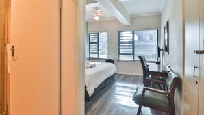 A hotel room with a bed, a desk, a chair, a ceiling fan, and two windows with blinds. - Spring Tide Inn - Standard king room 3 (Cape Town)