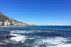A coastal cityscape with a prominent mountain, buildings along the shore, and rough sea waves.